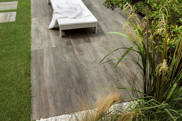 Close-up swatch of Cinder Wood Porcelain Paving, showing mixed grey tones and realistic wood-grain effect.***