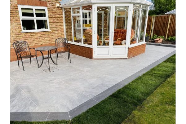 Garden patio using Gaja Grey 900x900 Porcelain Paving, with curved edge detail beside a conservatory.***
