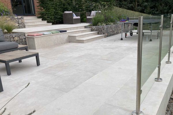 Egyptian Beige Limestone paving used on a multi-level garden terrace with steps, gabion walls, glass balustrading and outdoor seating.***