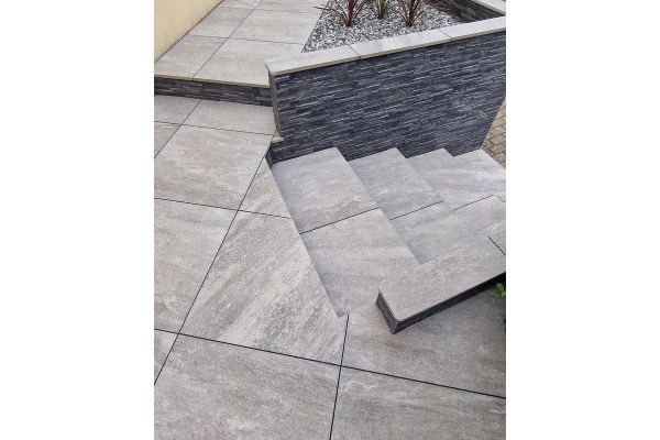 Tiered garden steps and patio area using Grey Quartz Porcelain Paving, bordered with a stone-clad retaining wall.***
