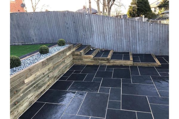 A tiered garden with Midnight Black Limestone paving, wooden steps, creating a modern outdoor space with crisp, clean lines.***
