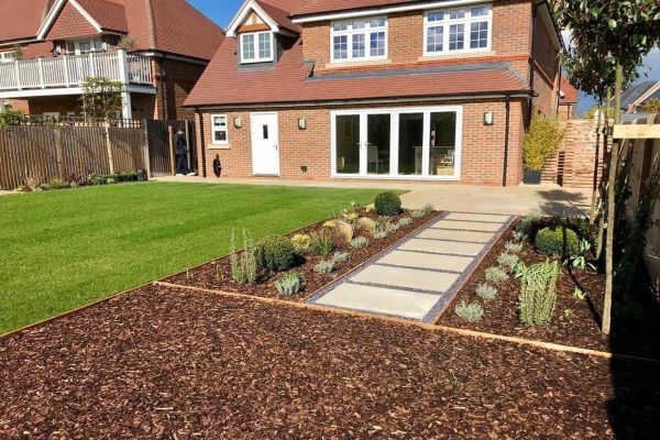 A large, open patio with Mint Smooth Sandstone paving and a decorative pathway through the lawn.***
